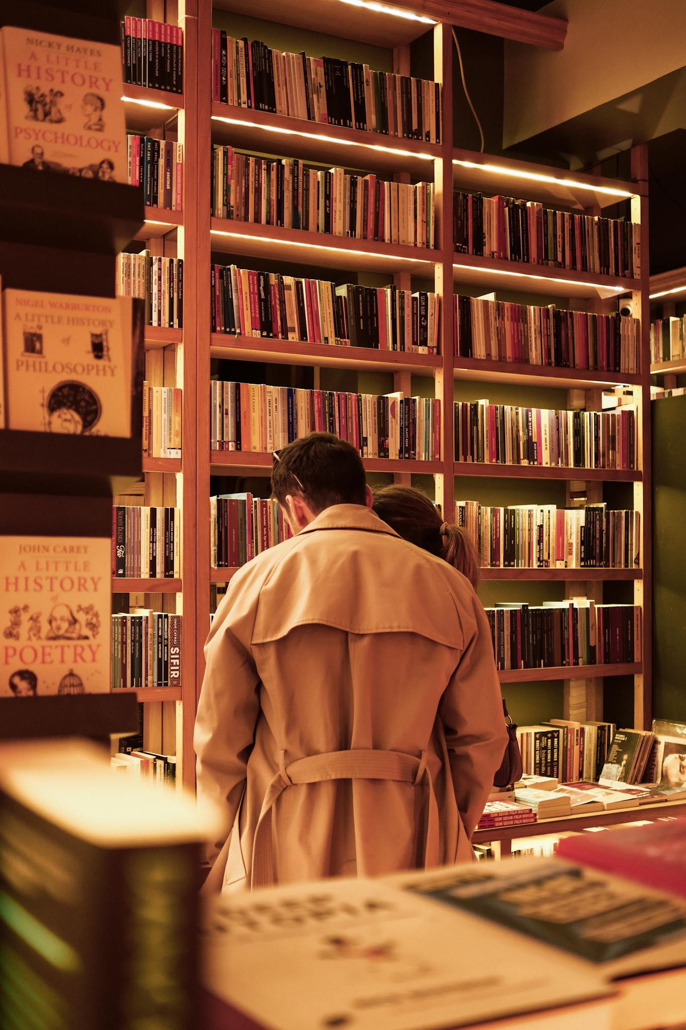 A couple browsing books in a warm, cozy bookstore filled with shelves of literature.