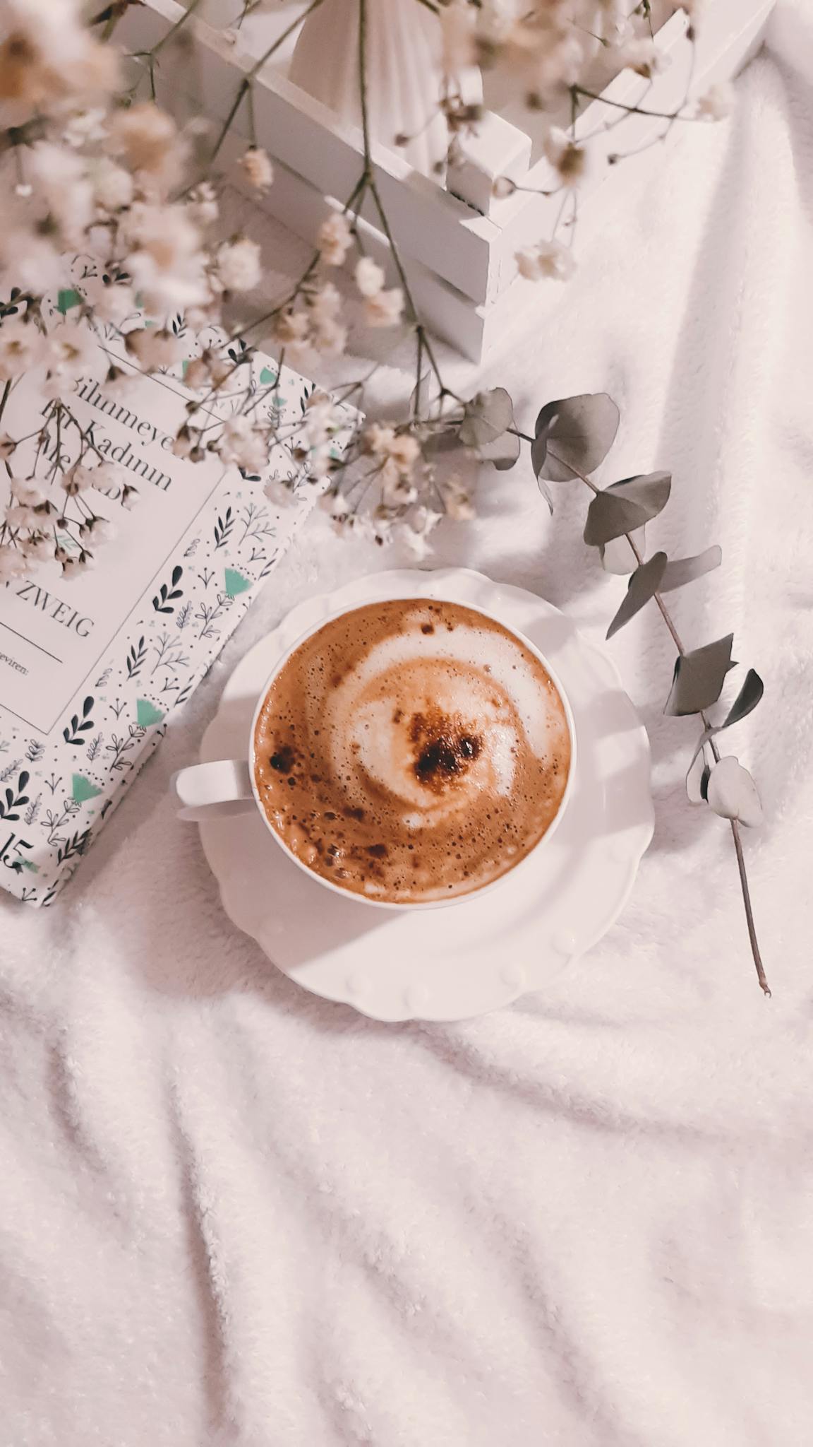 Aesthetic cappuccino cup with floral arrangements on a soft surface, perfect for a cozy morning vibe.