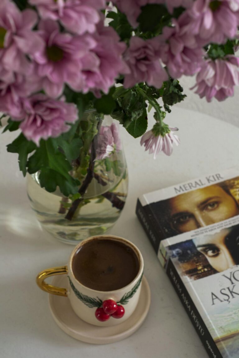 Artistic arrangement of coffee cup, book, and pink flowers on a table, creating a cozy and inviting atmosphere.