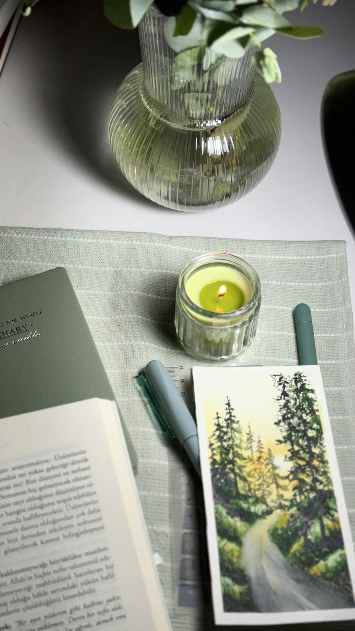 Inviting reading corner with books, candles, and a watercolor landscape on a table.