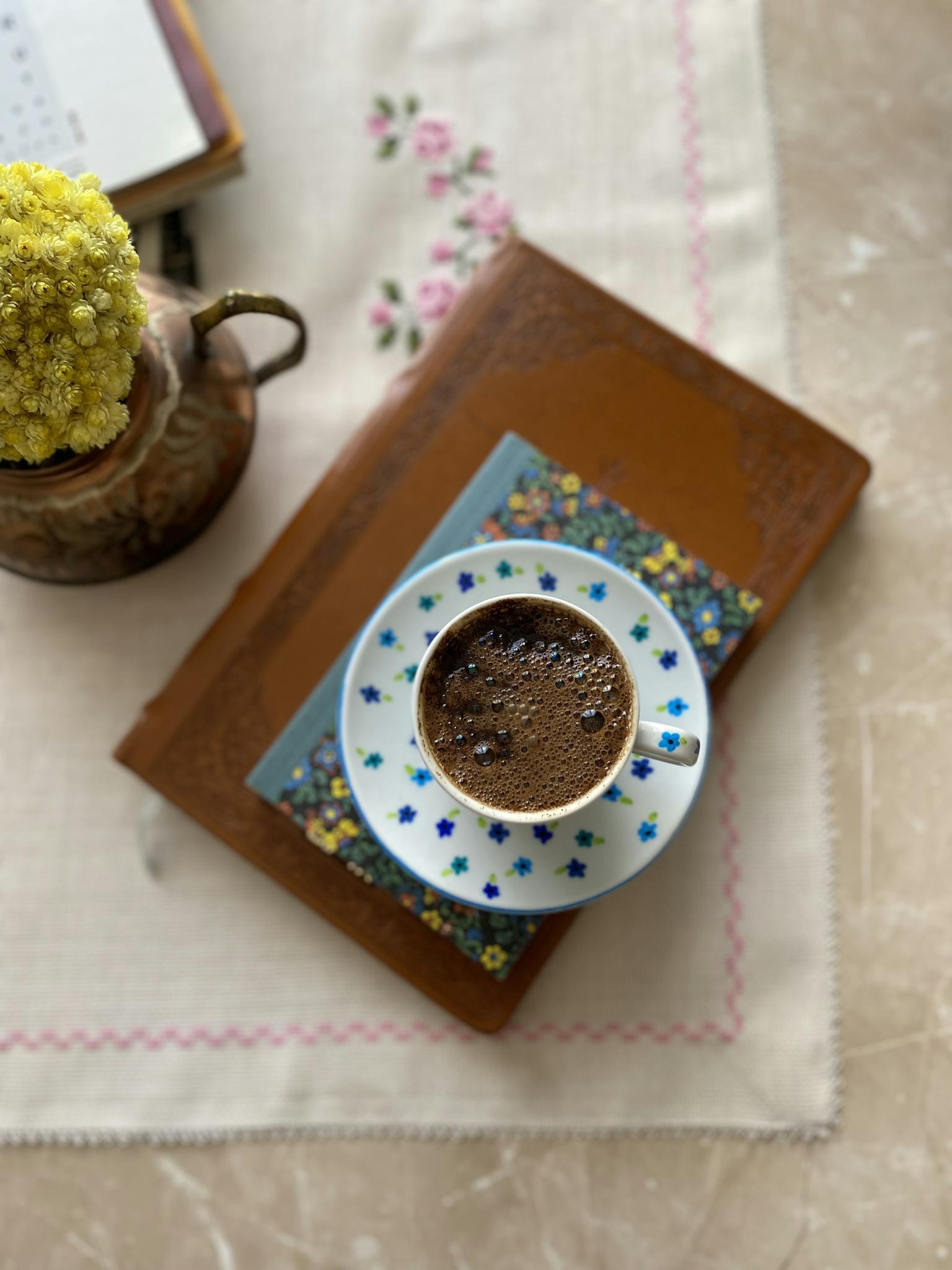 Top view of coffee in floral cup on book with a vase of flowers. Cozy and inviting.